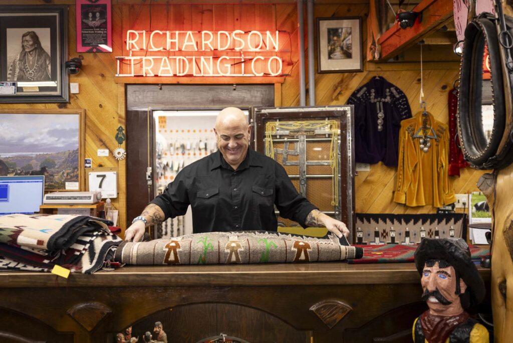 Trading post owner standing behind the counter displaying a hand-woven Navajo textile.